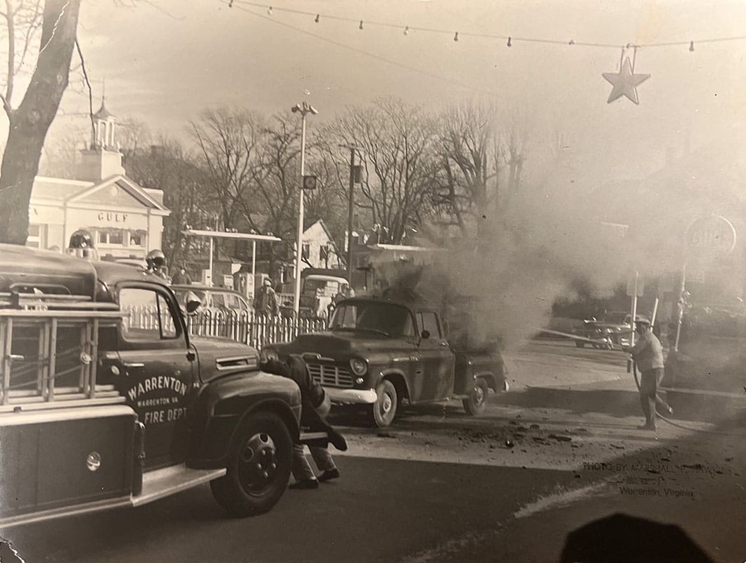 Old black and white photo of the Warrenton Volunteer Fire Company fighting a vehicle fire on Main Street in the 1950s